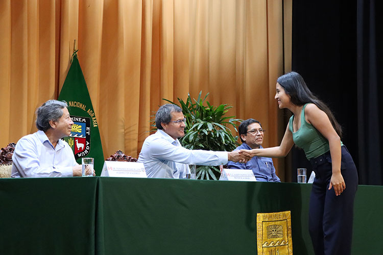 Rector de la UNALM saludando a alumna premiada en el escenario
