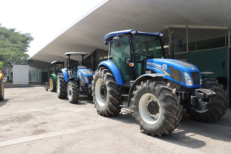 Mecanización agrícola: fila de tractores azules modernos estacionados bajo un cobertizo, representando el consumo energético del sector.
