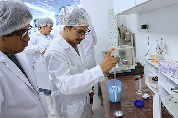 Estudiante en bata de laboratorio utiliza una pipeta para extraer muestras de leche durante una práctica de análisis de calidad
