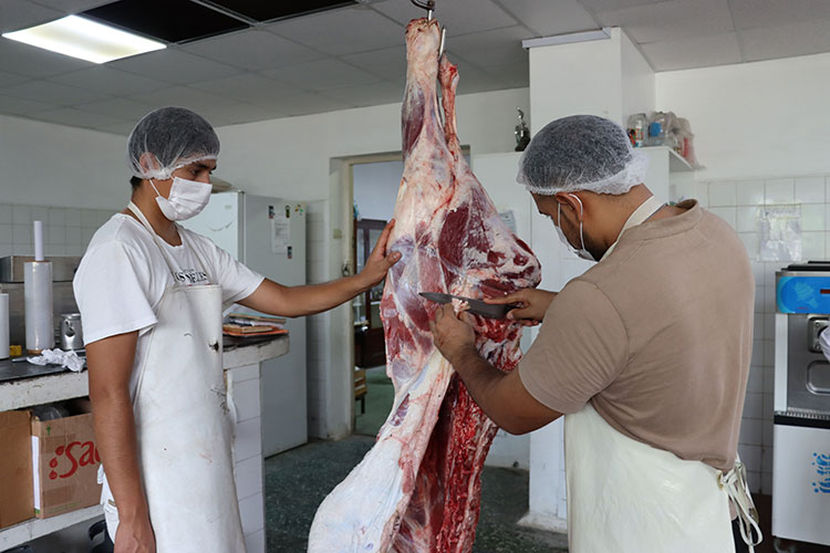 Dos estudiantes con equipo de protección realizan cortes y evaluación de una carcasa bovina en el laboratorio de productos cárnicos