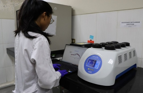 Analizadora de laboratorio muestra resultados en pantalla mientras investigadora manipula el equipo